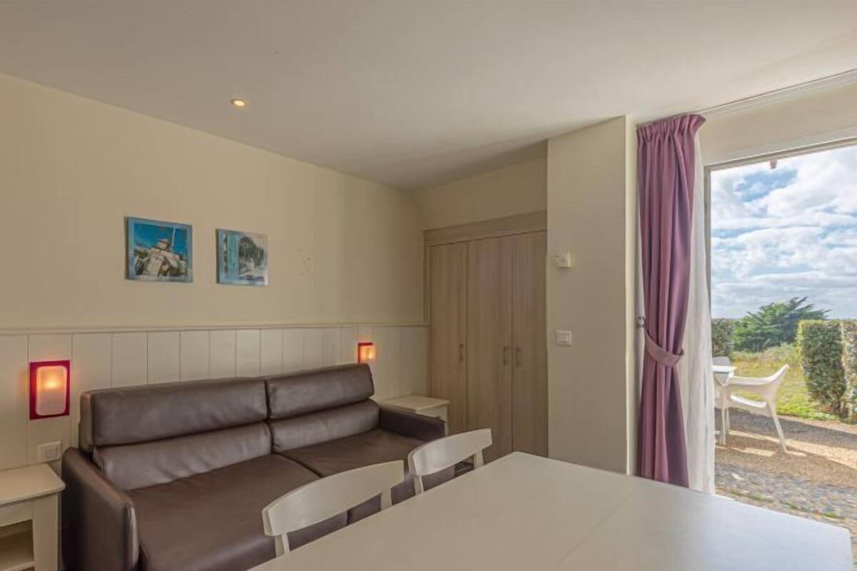 A room with a brown sofa, a white table, and a view through a window with a curtain.