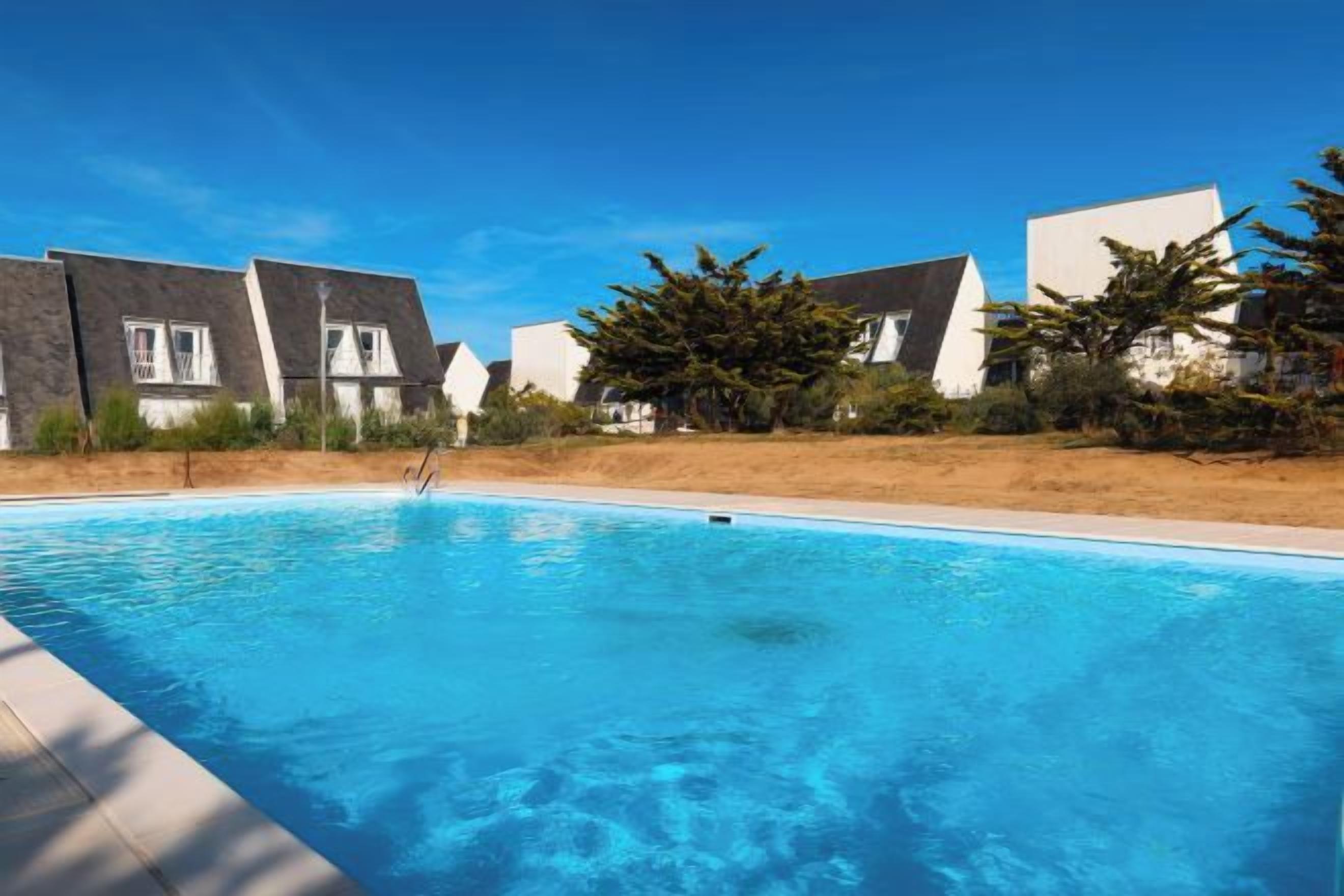 Een zwembad omringd door moderne huizen, met een helderblauwe lucht.