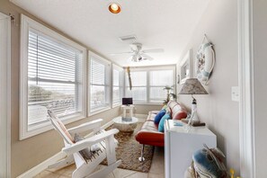 Relax in this spacious living room with a high ceiling fan, large windows, and comfortable seating options.