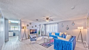 A modern living room with a blue sofa, a coffee table, and a TV. There is a ceiling fan, a floor lamp, and a window with curtains. - VIP villa 3BDR 2BHR 5min to the strip large pool (Las Vegas)