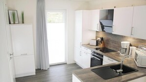 Une cuisine moderne avec des meubles blancs, un four encastré, un évier et une machine à café.