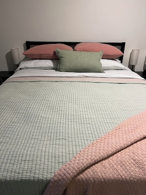 Una cama con edredón acolchado, almohadas y una lámpara de noche.