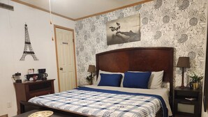 A neatly arranged bedroom with a bed, bedside tables, a coffee station, and a wall-mounted picture.