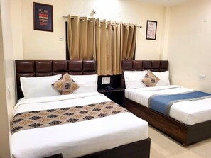 A hotel room with two beds, each with a headboard, a bedside table, and a lamp. - Hotel Krishnas (Amritsar)