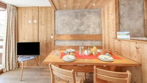 A wooden dining area with a table set for two, a television on a stand, and a view of the outdoors. - Cosy apartment for 4 people with WIFI, TV and balcony (Les Boisses)