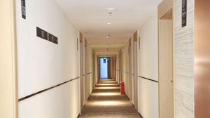 Un couloir d’hôtel avec un plancher en bois, des portes des deux côtés et une poubelle rouge au centre.