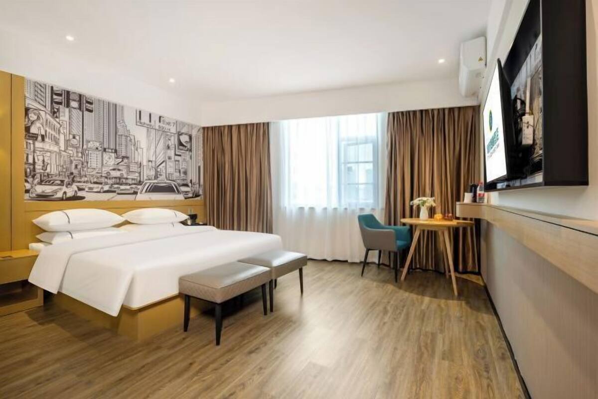 Una habitación de hotel con una cama grande, un escritorio, una silla y un amplio ventanal con cortinas.