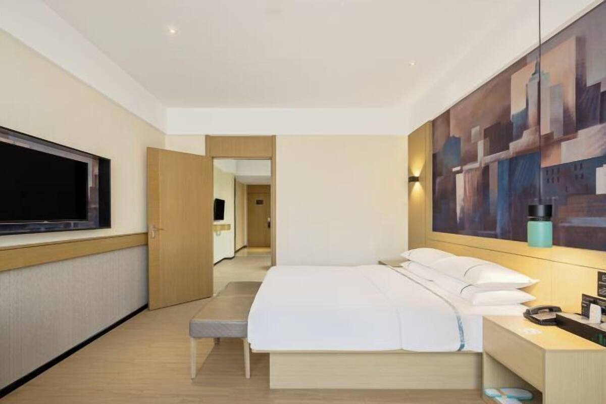 Habitación de hotel con cama, mesita de noche, televisor, obra de arte y puerta de baño.