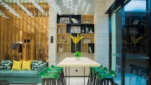 Un intérieur moderne comprenant un coin repas, des chaises vertes, un canapé avec des coussins à motifs et une cloison en bois avec des étagères.