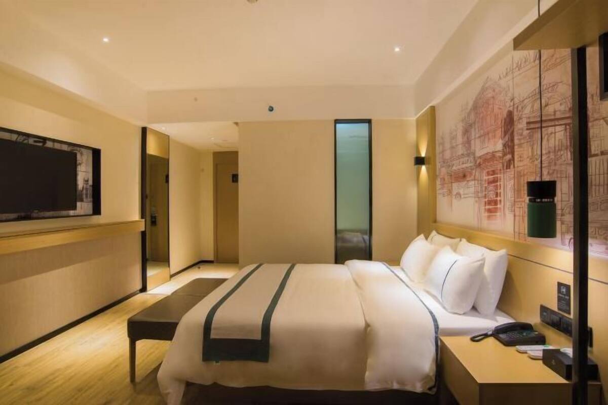 Habitación de hotel con una cama grande, mesita de noche y televisor montado en la pared.