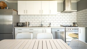 Una cocina compacta con armarios blancos, un refrigerador de acero inoxidable, un horno integrado y un lavavajillas.