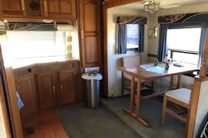 A compact RV kitchen with wooden cabinets, a stainless steel sink, and a dining area with a table and chairs.