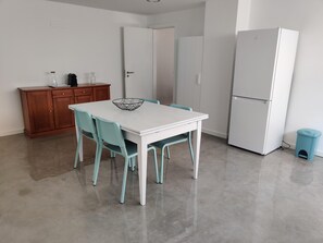 A kitchen with a white table, teal chairs, a wooden cabinet, and a white refrigerator.