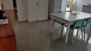 Une cuisine avec une table blanche, des chaises turquoise, une armoire blanche et un réfrigérateur gris.
