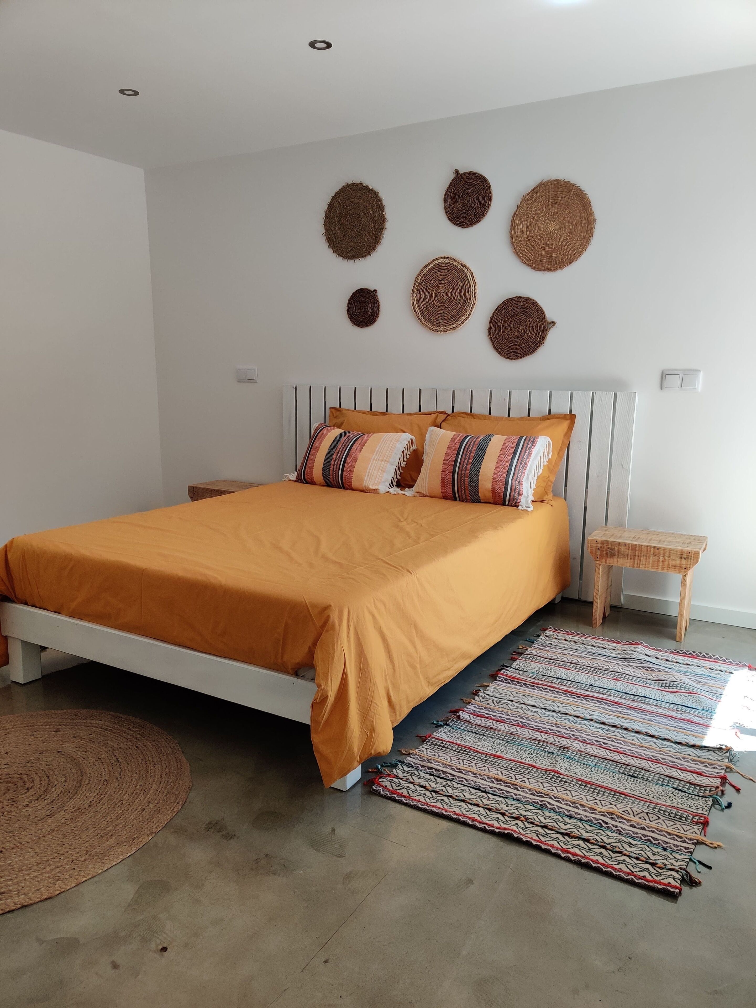 Een slaapkamer met een bed, een nachtkastje, een vloerkleed en geweven wanddecoraties.