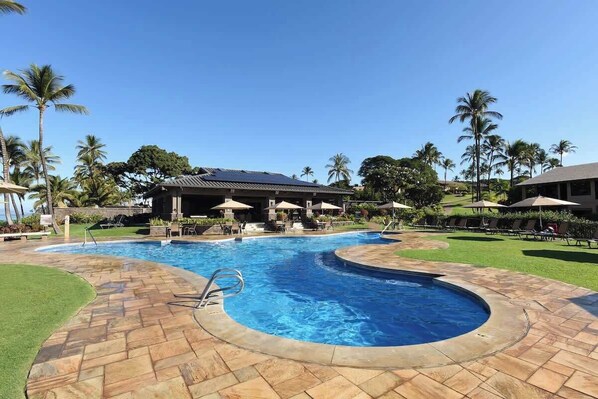 A swimming pool with a curved design, surrounded by a paved area with lounge chairs and umbrellas.
