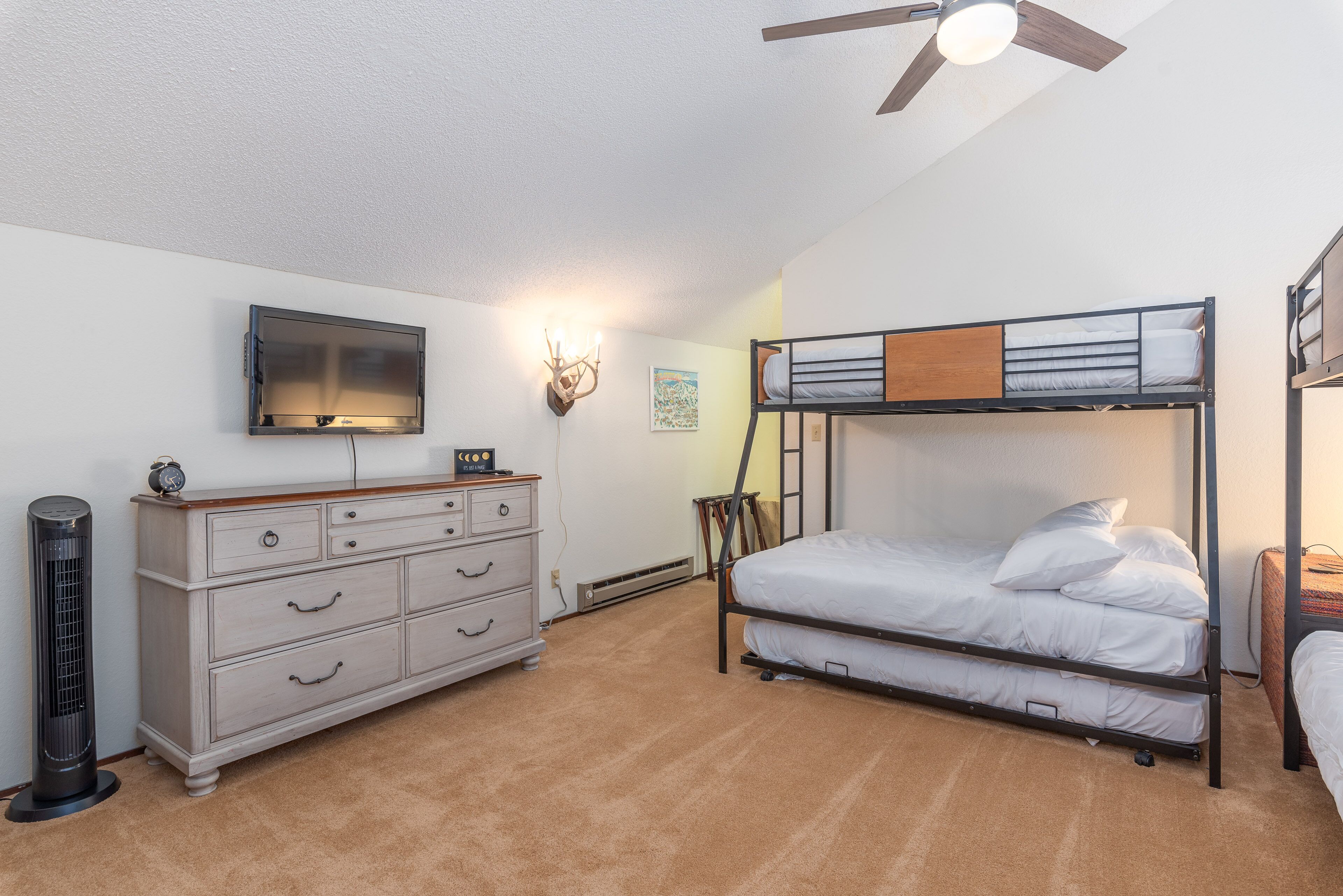 Un dormitorio con literas, cómoda, televisor de pantalla plana, calefactor y ventilador de techo.