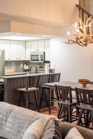 A modern kitchen with a central island, dark wooden chairs, and a chandelier.