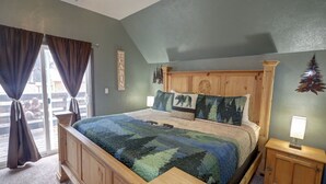 Une chambre à coucher avec un grand lit, une tête de lit en bois et une vue sur l’extérieur par une fenêtre agrémentée de rideaux.