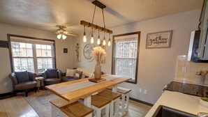 Une cuisine chaleureuse avec une table en bois, des tabourets blancs et des luminaires suspendus.