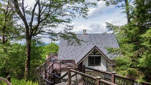 Eine Holzhütte mit einem Steinkamin, umgeben von üppigem Grün und einer Holzterrasse.