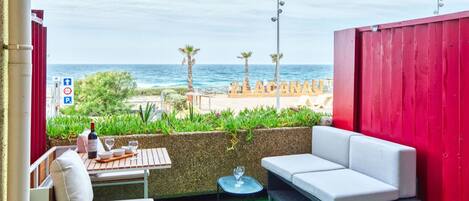 A balcony with a view of the sea, a table with a bottle of wine, and a sofa.