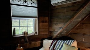 A cozy room with a white sofa, a small table with a lace tablecloth, a window with decorative ironwork, and an air conditioning unit mounted on the wall. - COUNTRY LACE Retro Place (Cabool)