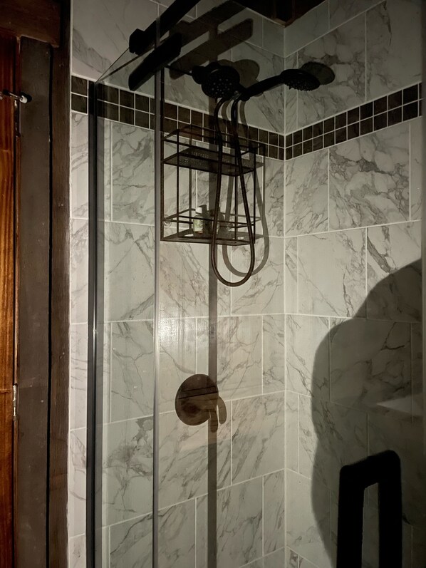 A shower area with a glass door, a marble-tiled wall, and a wooden door frame.
