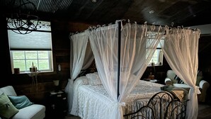 A bedroom with a four-poster bed, a wooden headboard, a white sofa, and a large window with a view of the outdoors. - COUNTRY LACE Retro Place (Cabool)