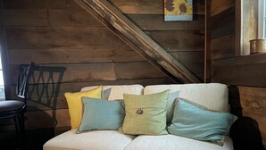 A wooden cabin interior with a white sofa adorned with colorful pillows, a wooden chair, and a rustic wooden ceiling. - COUNTRY LACE Retro Place (Cabool)