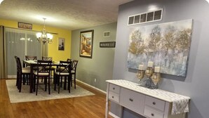A dining area with a wooden table and chairs, a white console table with drawers, a chandelier, and a painting on the wall. - Great Living Too (Berrien Springs)