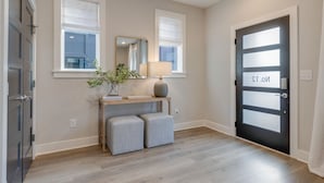 Un pasillo con suelo de madera, una puerta negra con un panel de vidrio esmerilado y una mesita con una lámpara y una planta.