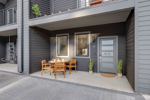 A modern two-story building with a grey exterior, a balcony with a metal railing, and a front door labeled "No. 12".
