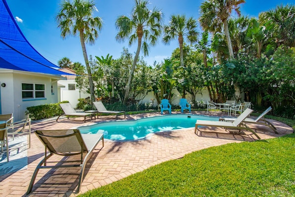A pool area with lounge chairs, a blue canopy, and palm trees.