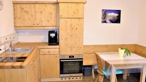 Kompakti keittiö, jossa on puukalusteet, sisäänrakennettu uuni sekä pieni ruokailutila, jossa on pöytä ja tuoli.