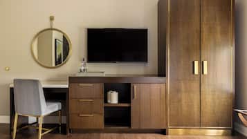 A modern bedroom with a wooden wardrobe, a desk with a chair, a television, and a round mirror.