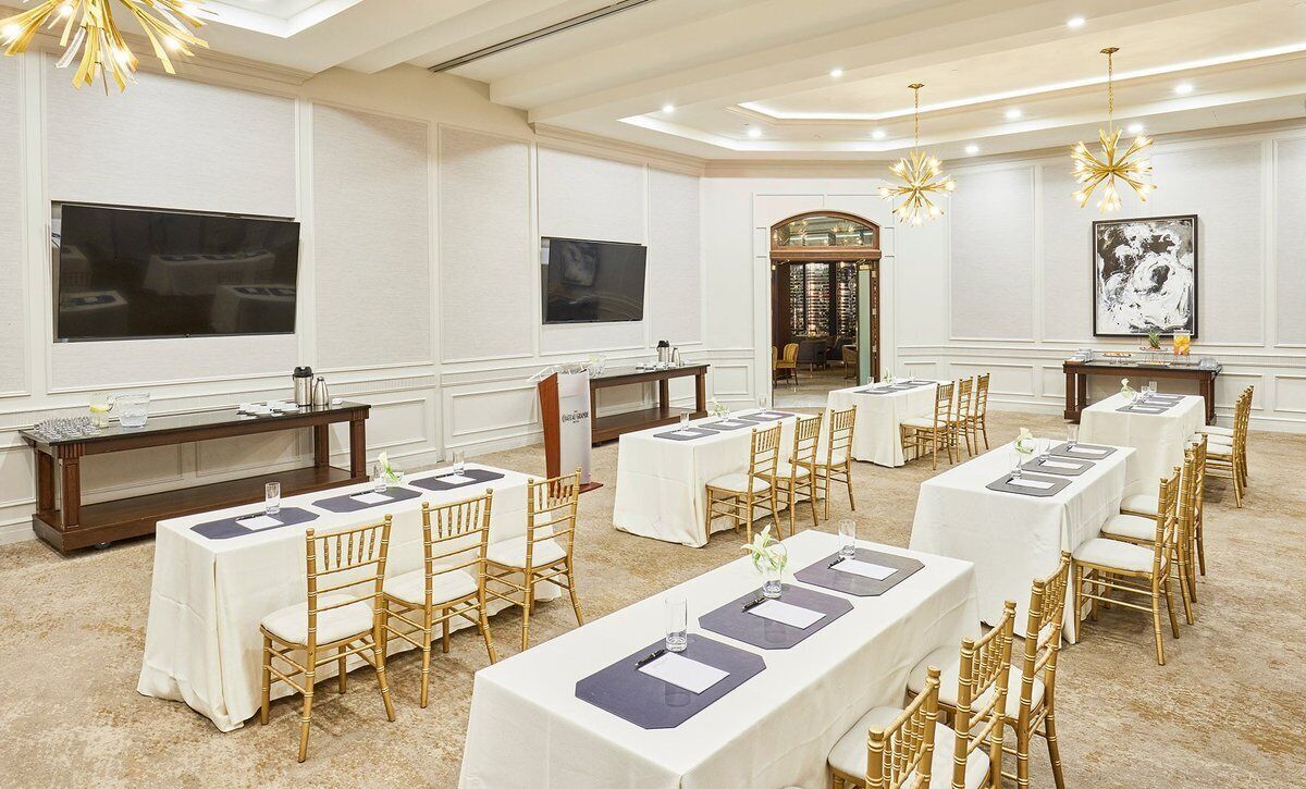 Uma sala de banquetes com várias mesas, cadeiras e uma tela de televisão.