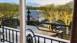 Ein Balkon mit Blick auf eine Straße, ein Gebäude mit blauem Dach und Bäume mit gelben Lichtern.