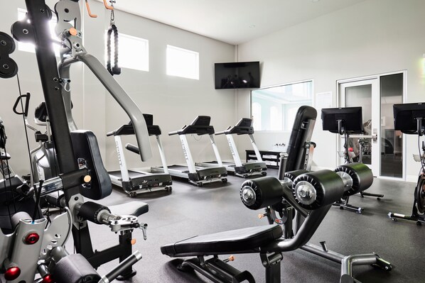 Un gimnasio con cintas de correr, máquinas de pesas y un televisor en la pared.
