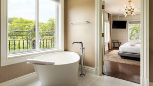 Ein modernes Badezimmer mit einer freistehenden Badewanne, einer Dusche und einem großen Fenster mit Blick auf Grünflächen.