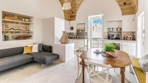 A cozy living room with a grey sectional sofa, a wooden dining table with chairs, and a kitchen in the background. - Mare Mare Mare (Gallipoli)