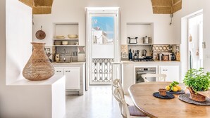 A modern kitchen with white cabinets, a wooden dining table, and a view through an open door. - Mare Mare Mare (Gallipoli)