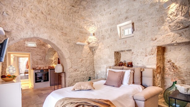 Ein Schlafzimmer mit Steinwand, einem Bett mit Kissen, einem Nachttisch und einer Lampe.