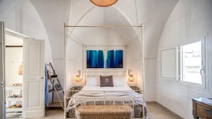 A bedroom with a four-poster bed, a painting above the bed, two bedside lamps, a wicker bench, and a view through the window. - Il Nido Gallipoli (Gallipoli)