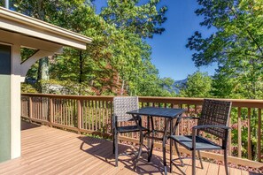 Une terrasse avec une table et deux chaises, entourée d’une balustrade en bois et d’une végétation luxuriante.