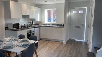 A modern kitchen with white cabinets, a dining area with a table set for six, and a view of the outside through a window.