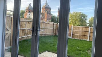 A view through a glass door to a backyard with a wooden fence, a grassy lawn, and a brick building with domed roofs in the background.