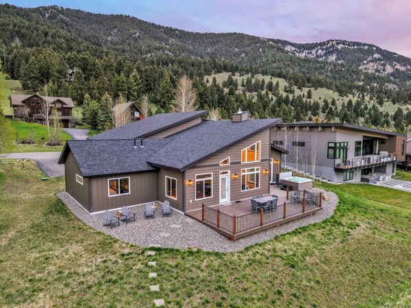 A modern two-story house with a deck, surrounded by a mountainous landscape.