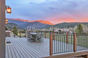 Une terrasse en bois avec des sièges d’extérieur, une rambarde en métal et une vue sur les montagnes.