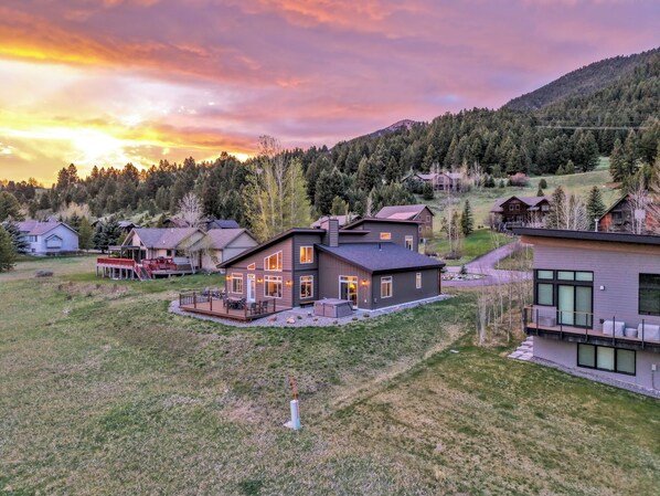 Une maison moderne dotée d’une terrasse, entourée d’une pelouse et bordée d’une colline boisée.